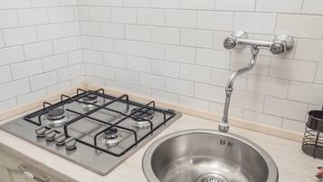 Una cocina con estufa a gas, pileta de acero inoxidable y salpicadero de azulejos blancos.