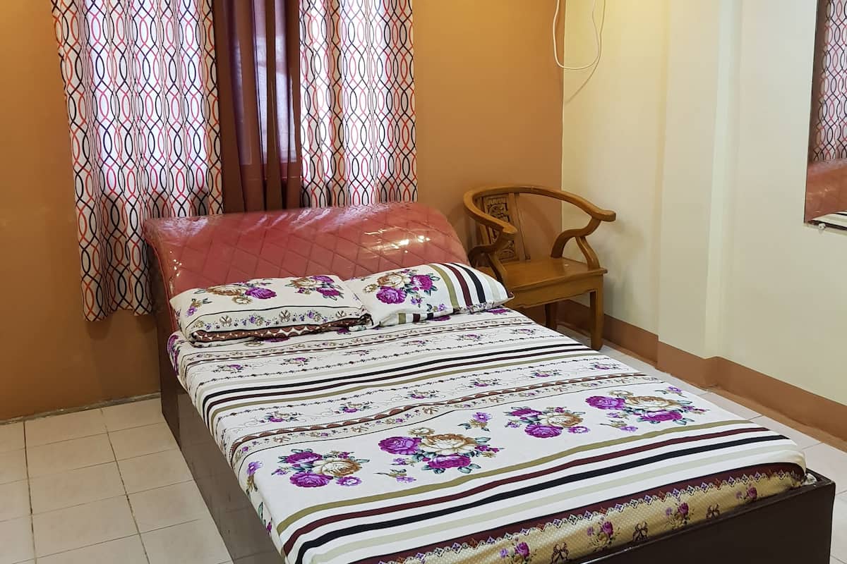 A bedroom with a bed, curtains, an air conditioning unit, a chair, and a wall-mounted mirror.