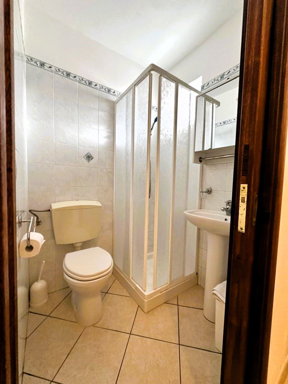 A bathroom with a toilet, shower enclosure, sink, and tiled walls.