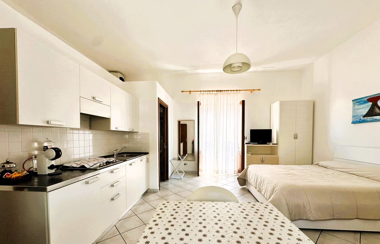 Habitación de hotel pequeña con kitchenette, una cama, televisión y un cuadro en la pared.
