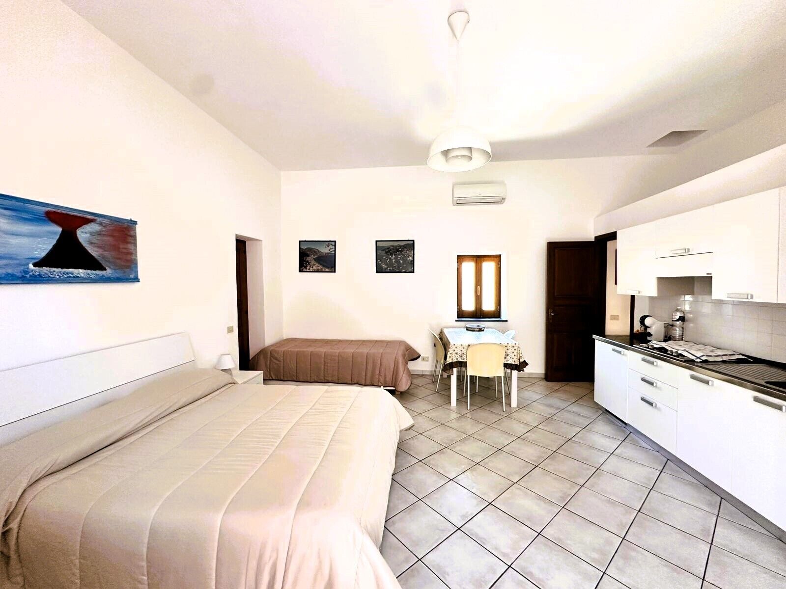 A bedroom with a bed, a desk with a chair, a kitchenette, and a bathroom door.