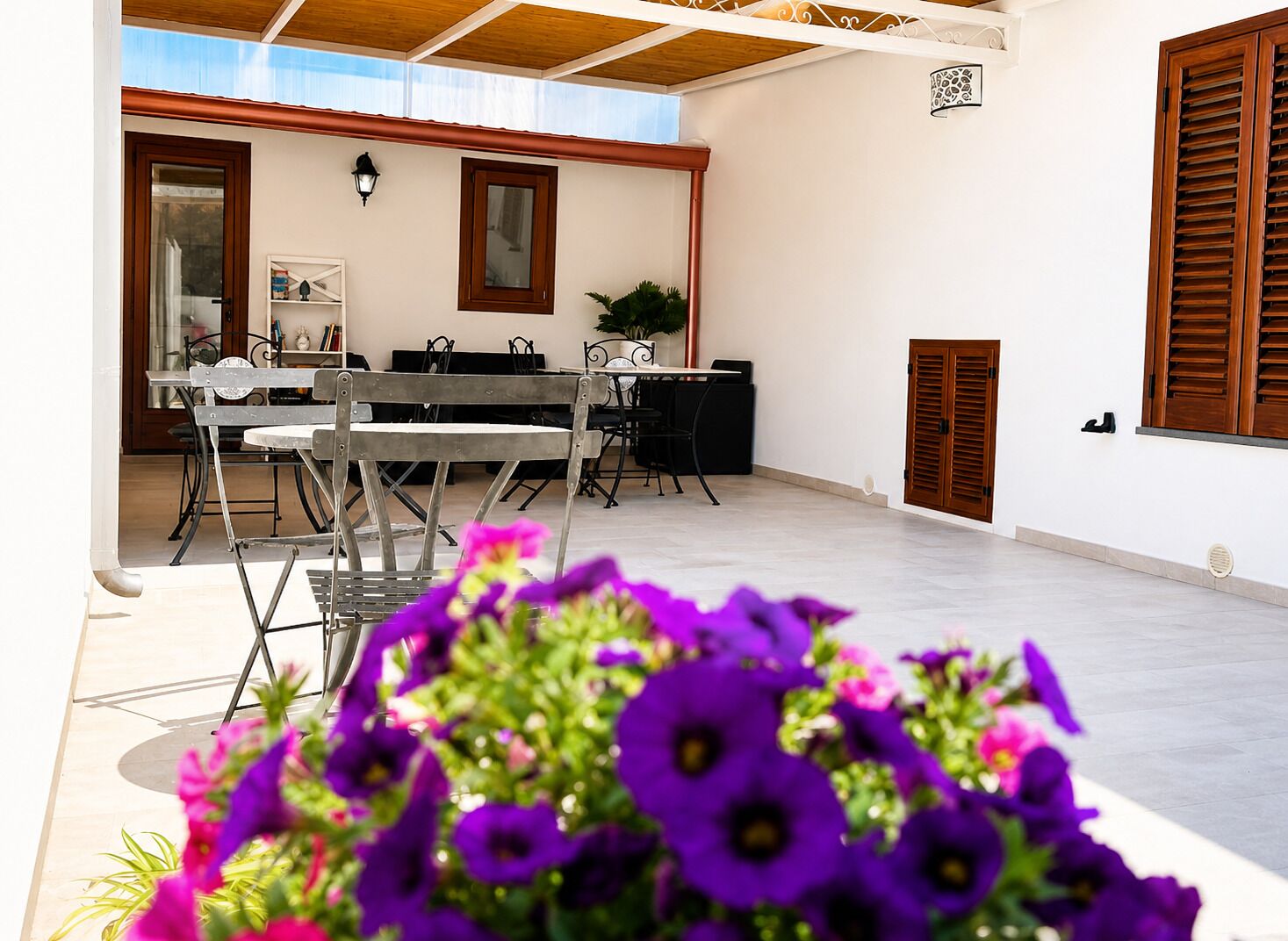 Una veranda esterna con zona pranzo, una porta in legno e un punto luce fissato al muro.