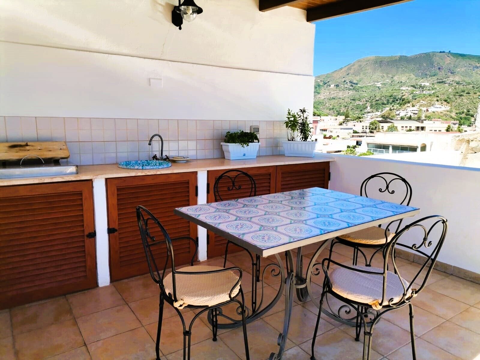 A balcony with a tiled floor, a table with chairs, a sink, and potted plants.