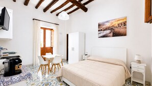 Un dormitorio con cama, mesita de noche, escritorio con silla, ventana con cortinas y un cuadro en la pared.