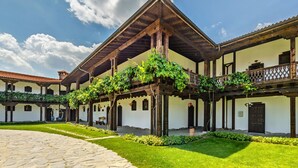 Un cortile con un vialetto in pietra, una pergola in legno con piante rampicanti e un edificio con tetto in tegole e balconi.