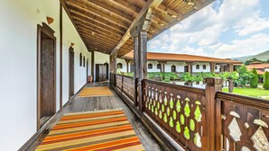 Un corridoio coperto con ringhiere in legno e tappeti a righe, che conduce a un edificio con tetto in tegole e vegetazione.