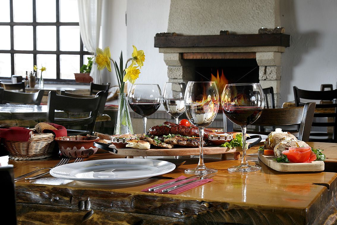 Una mesa de comedor dispuesta con platos, cubiertos, copas de vino y una variedad de alimentos, incluyendo pan, carne y verduras.