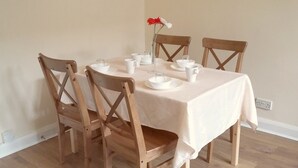 Une table à manger dressée avec de la vaisselle blanche et des chaises, un vase rempli de fleurs et une prise de courant sur le mur.