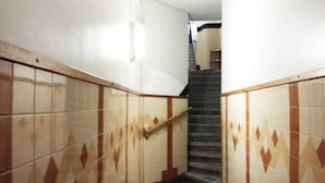 Un couloir étroit, orné de carreaux décoratifs et muni d’une main courante, qui mène à un escalier.