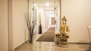 Un couloir orné d’une statue de Bouddha, d’un vase en verre contenant des branches et recouvert d’un tapis.
