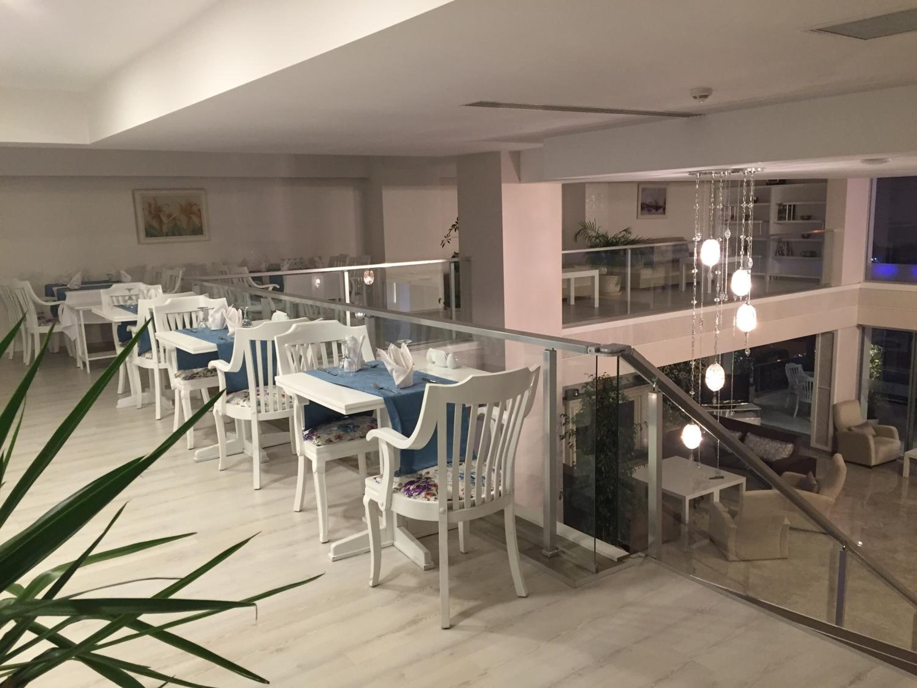 Un comedor moderno con mobiliario blanco, barandilla de cristal y una escalera que sube a un nivel superior.