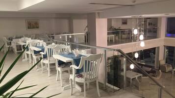 Un comedor moderno con mobiliario blanco, barandilla de cristal y una escalera que sube a un nivel superior.