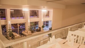 Un espace repas doté d’un plafond haut, de lustres et offrant une vue sur l’espace extérieur aménagé pour les repas.