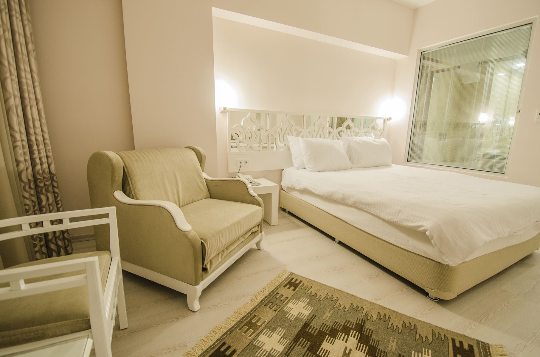 A hotel room with a bed, a chair, a nightstand, a lamp, and a window.