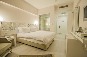 A hotel room with a bed, bedside table, a desk with a chair, a mirror, and a television.