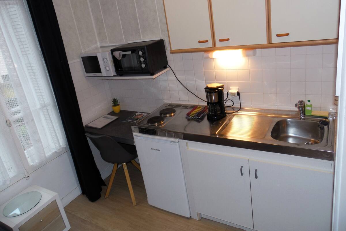 Ett kompakt kök med vita skåp, en mikrovågsugn, en kaffebryggare och ett handfat.