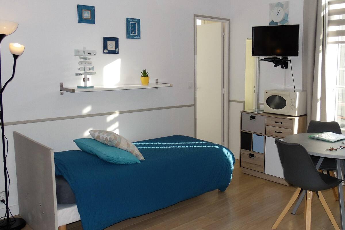 Ett rum med en säng, ett skrivbord, en stol, en tv och en hylla med dekorativa föremål.