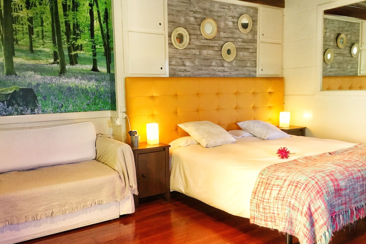 A hotel room with a bed, a nightstand, a lamp, and a painting of a forest.