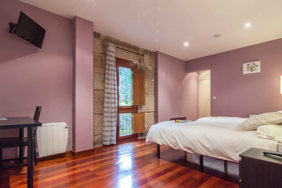 A bedroom with a bed, a desk, a chair, a TV, and a window with curtains.
