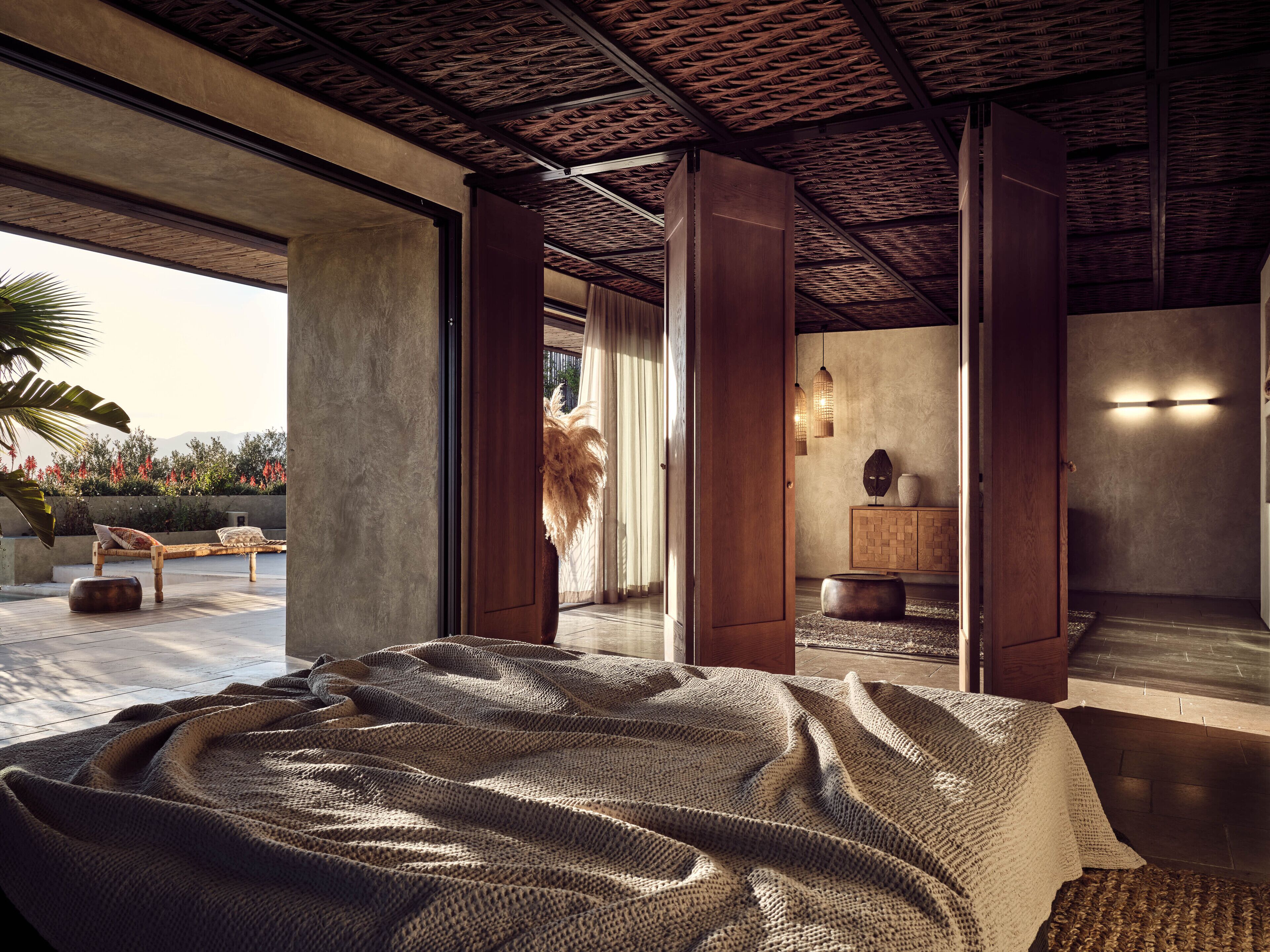 A spacious bedroom with a large bed, a wooden wardrobe, and a view of a landscaped garden.
