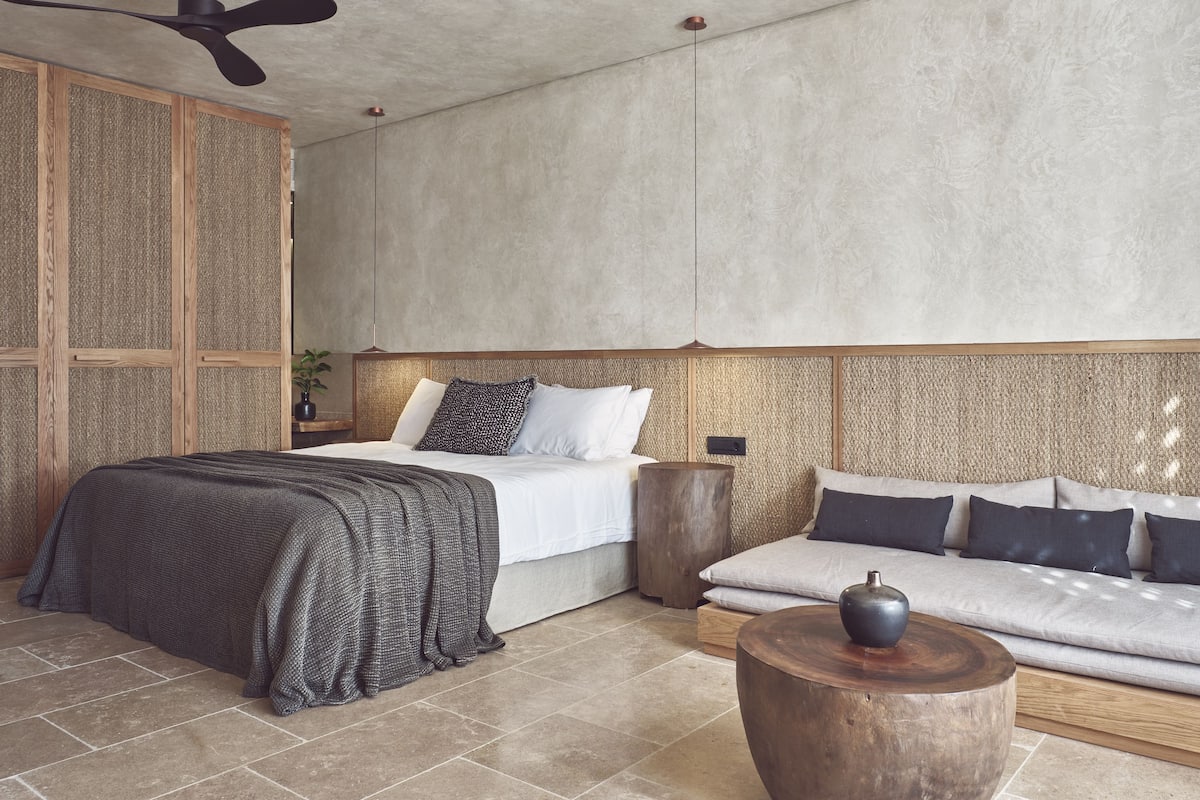 A modern bedroom with a large bed, a sofa, a wooden coffee table, and a ceiling fan.