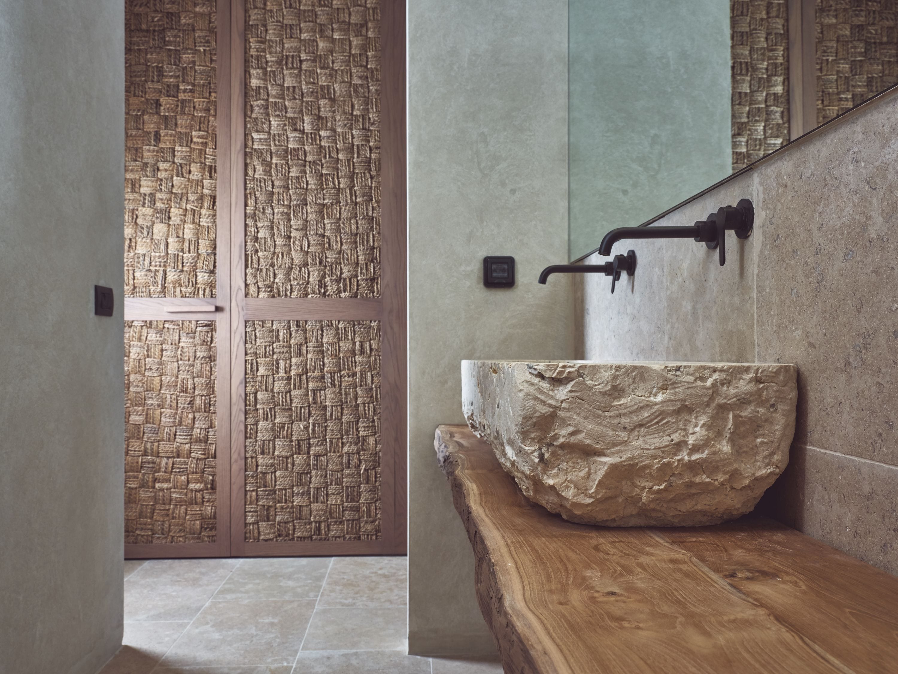 A bathroom with a stone sink, a wooden countertop, and a woven partition.