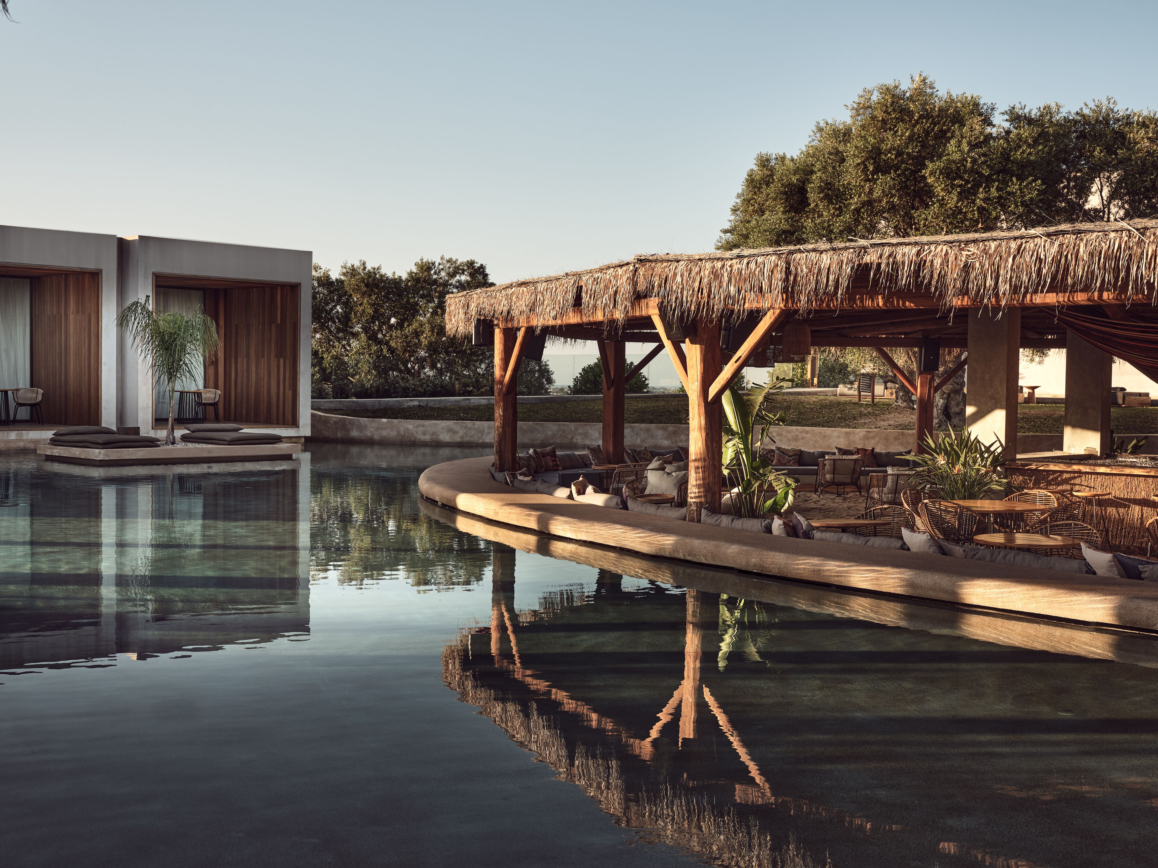 A pool area with a thatched-roof structure, lounge seating, and a modern building in the background.