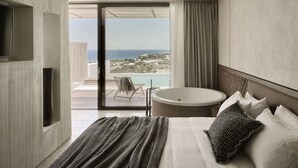 Una habitación de hotel moderna con una cama grande, una bañera redonda y un balcón con vistas al mar.