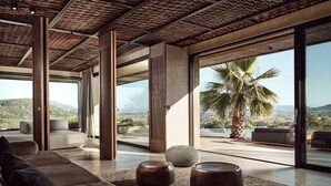 A modern interior with large windows, a sofa, and a palm tree view. - Olea All Suite Hotel, a Member of Design Hotels (Zakynthos)