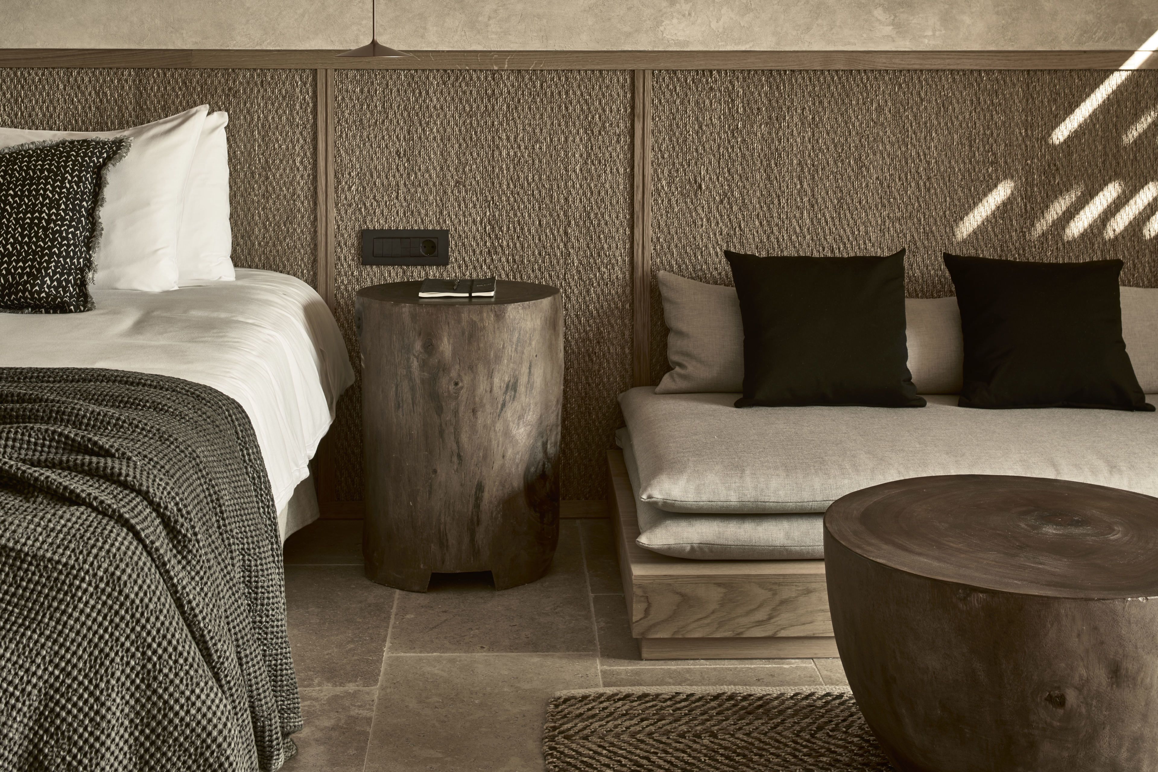 Un dormitorio moderno con una cama, dos mesitas de noche, un banco y una pared con textura.