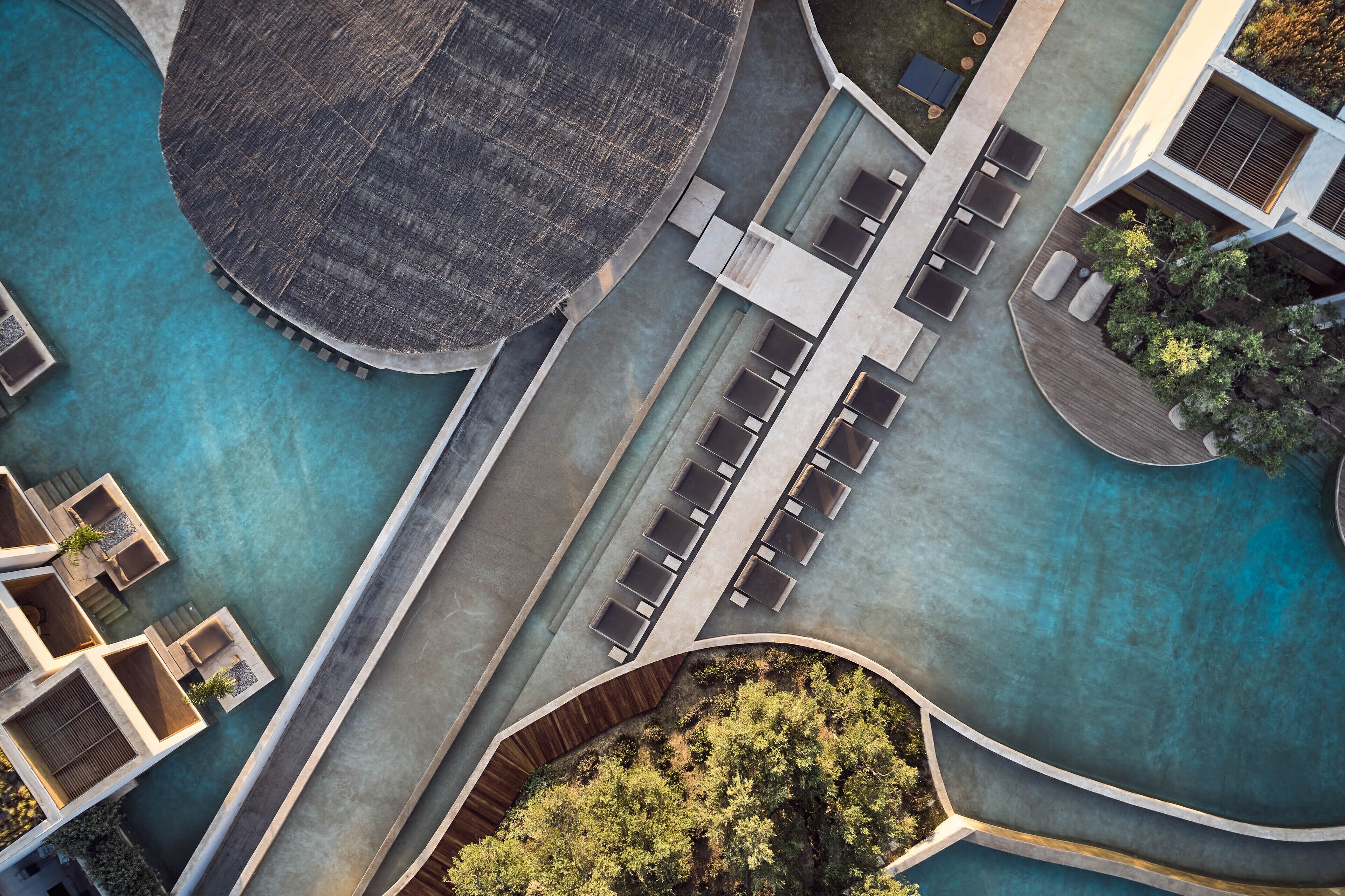 An aerial view of a modern hotel with a central pool, outdoor seating areas, and a landscaped garden.
