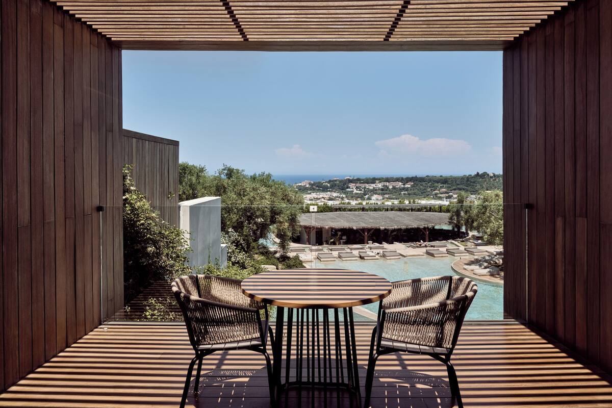 A wooden deck with a table and chairs overlooking a pool and a scenic view.