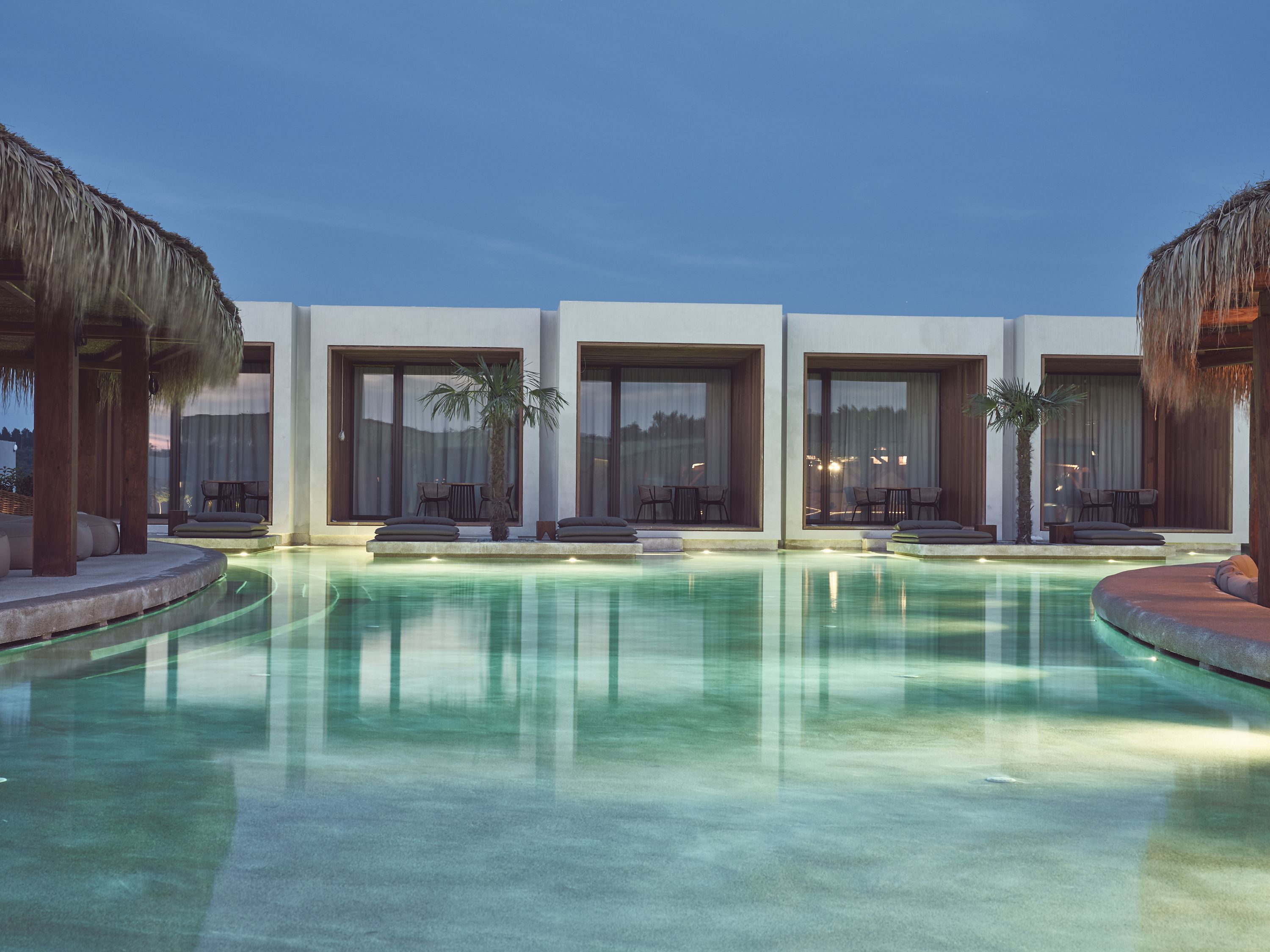 A modern resort with a swimming pool, large windows, and outdoor seating areas.