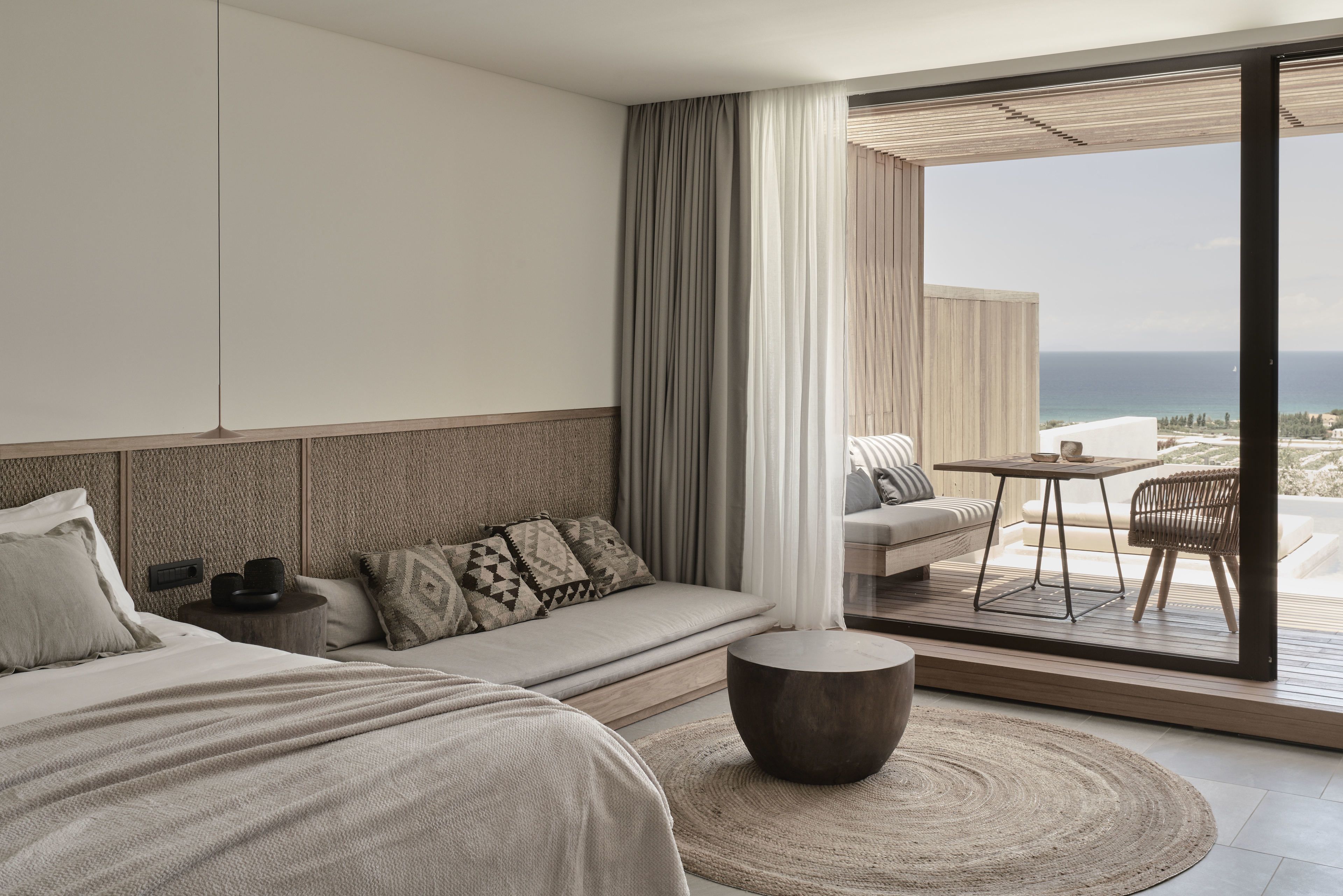 A modern hotel room with a large bed, a sofa, a small table, and a view of the ocean.