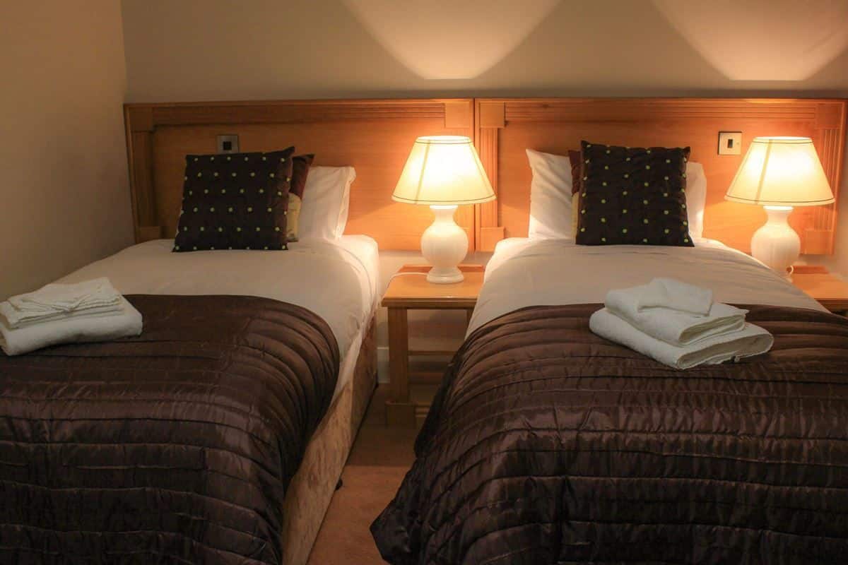 A hotel room with two beds, each with a wooden headboard, a nightstand, and a lamp.