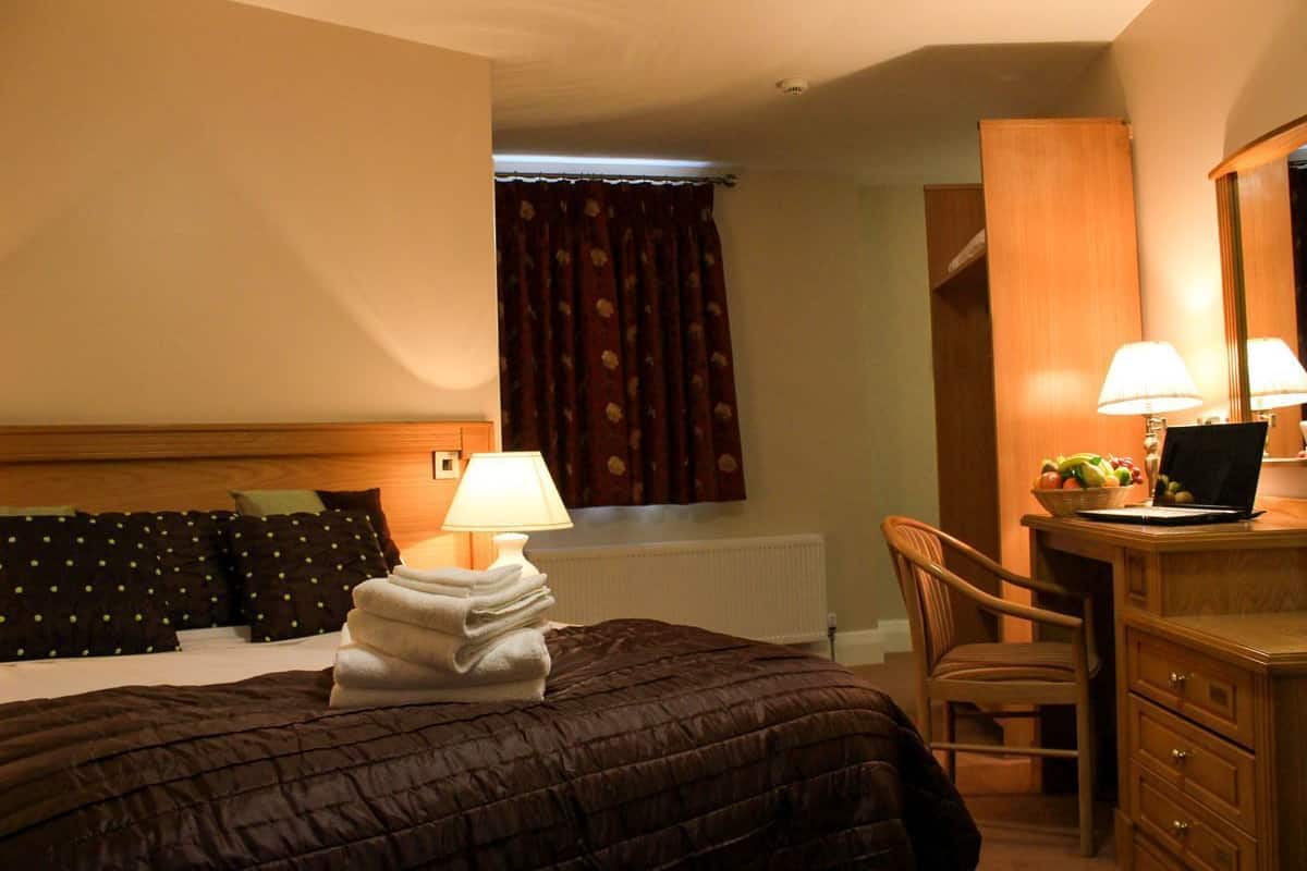A hotel room with a bed, a desk with a laptop, a chair, and a radiator.