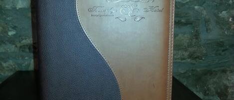 A leather-bound book with embossed text on the cover, placed on a dark wooden surface against a stone wall background.