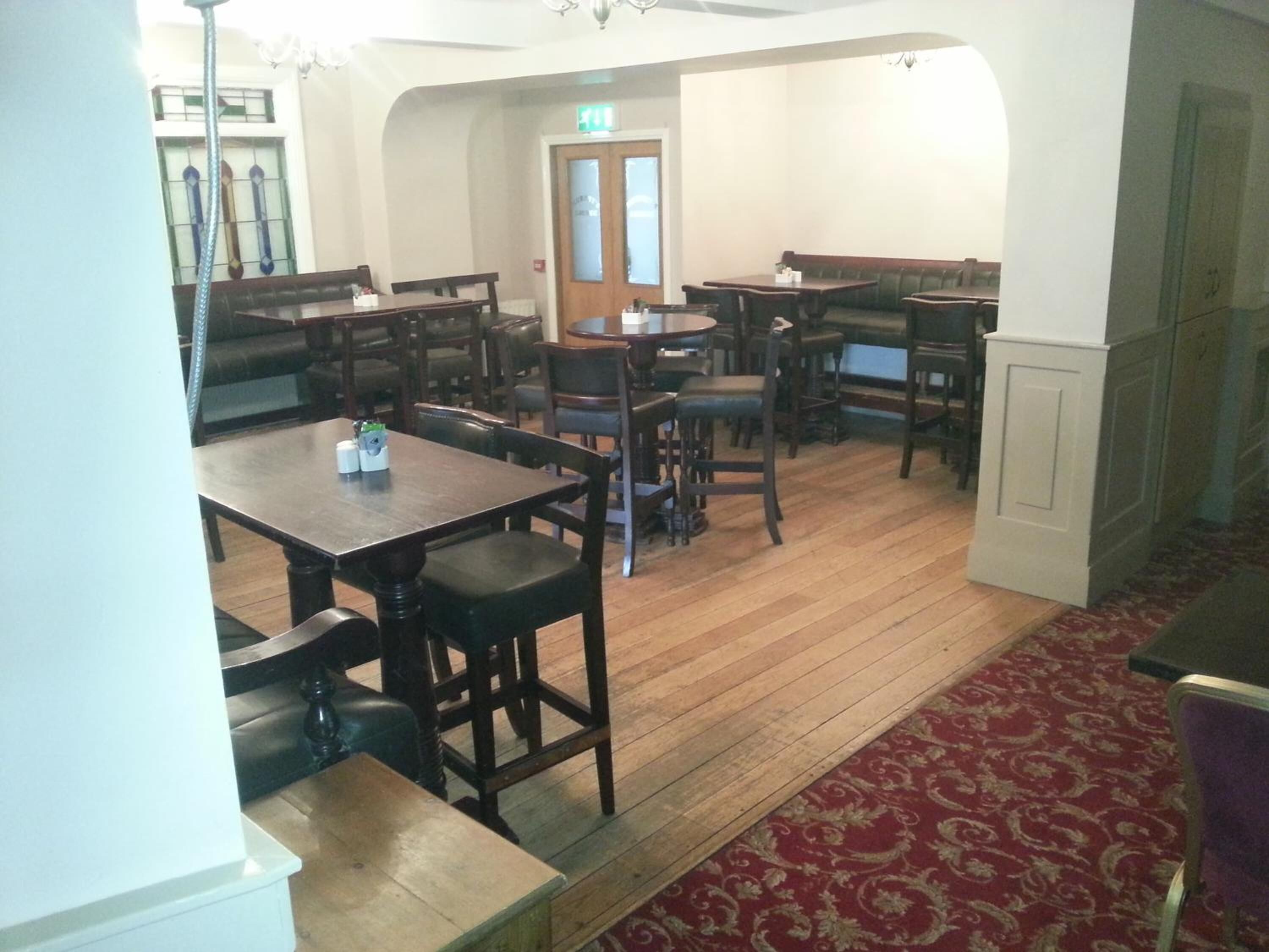 A dining area with wooden tables and chairs, a patterned carpet, and a door with a glass panel.