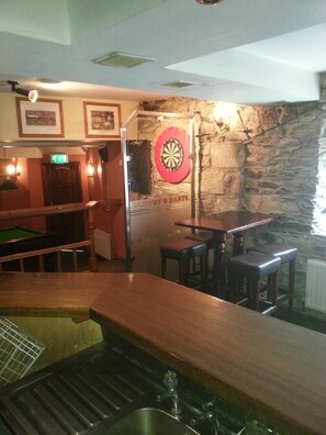 A bar area with a dartboard, pool table, and stools.