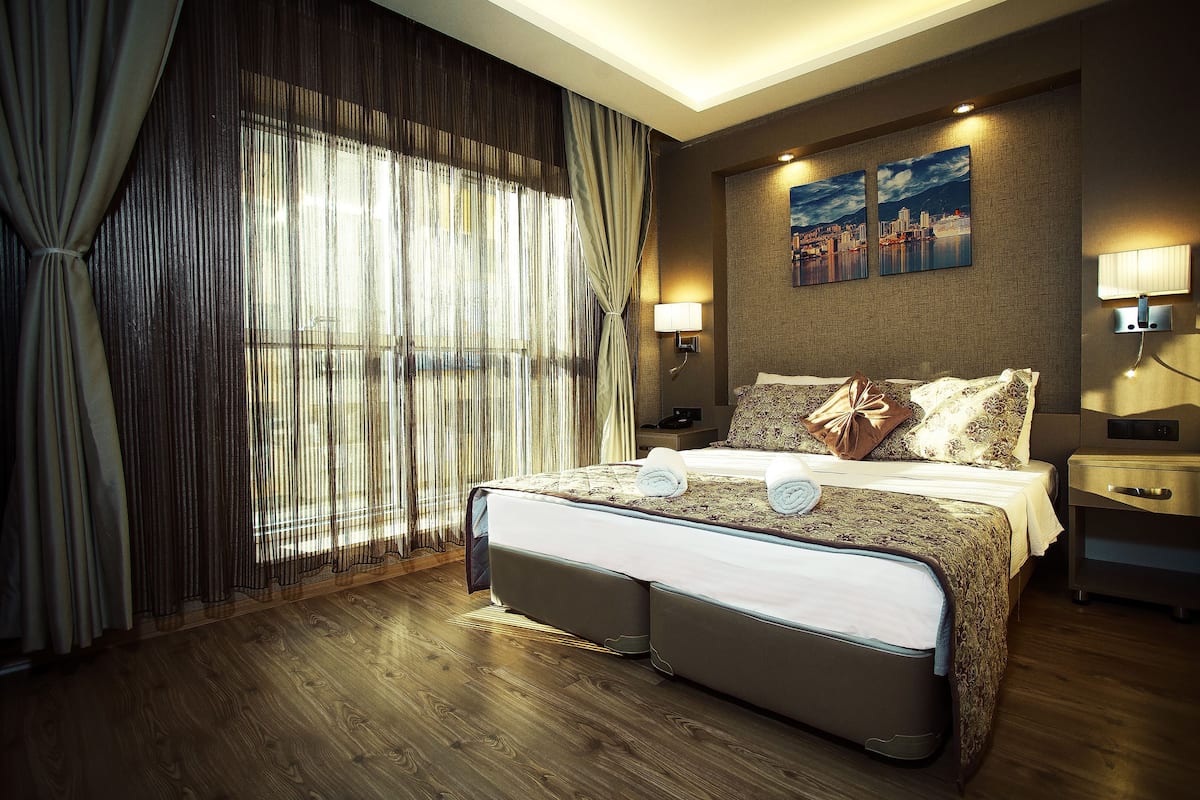 A hotel room with a large bed, a nightstand, a lamp, and a cityscape painting on the wall.