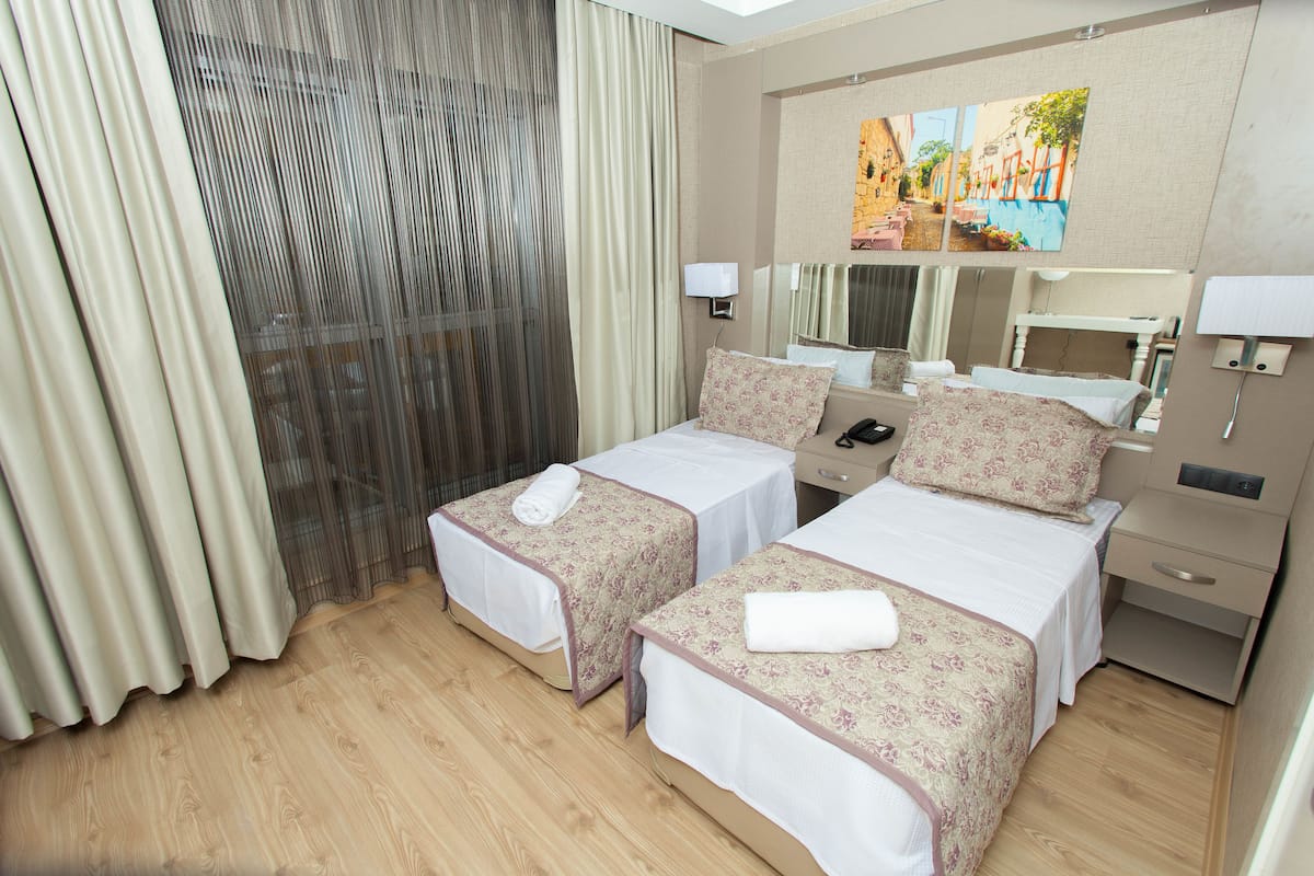 A hotel room with two single beds, a large mirror, a bedside table with a lamp, and a painting on the wall.