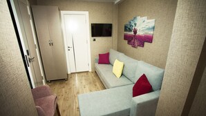 A living room with a grey sofa, a pink chair, a wooden floor, a white door, and a TV on the wall. - Hotel Iz (Izmir)