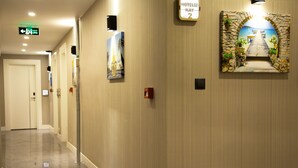 A hotel hallway with a polished floor, a directional sign, and a wall-mounted picture of a scenic pathway. - Hotel Iz (Izmir)