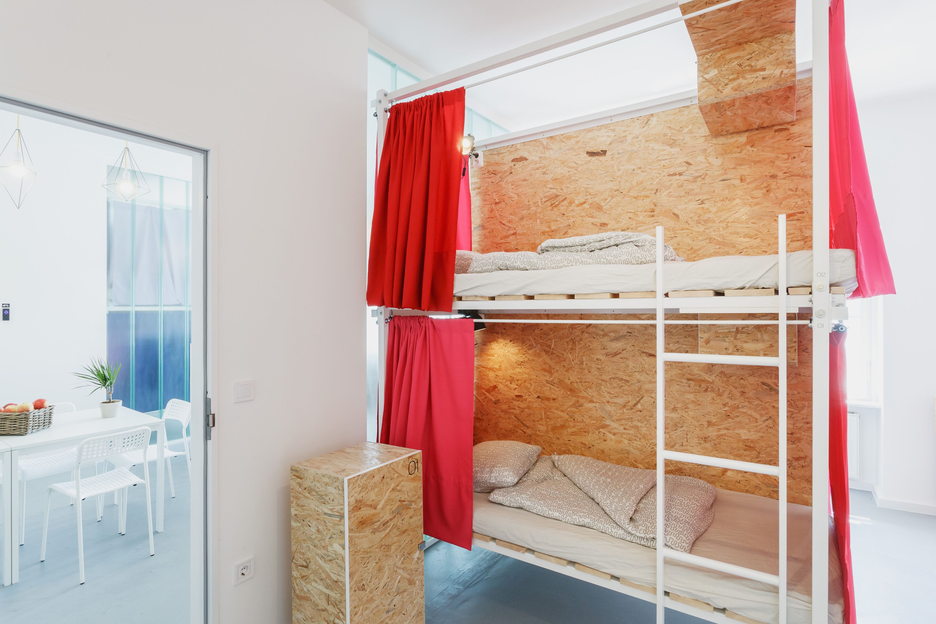 A bunk bed room with a wooden wall, a dining table with chairs, and a potted plant.