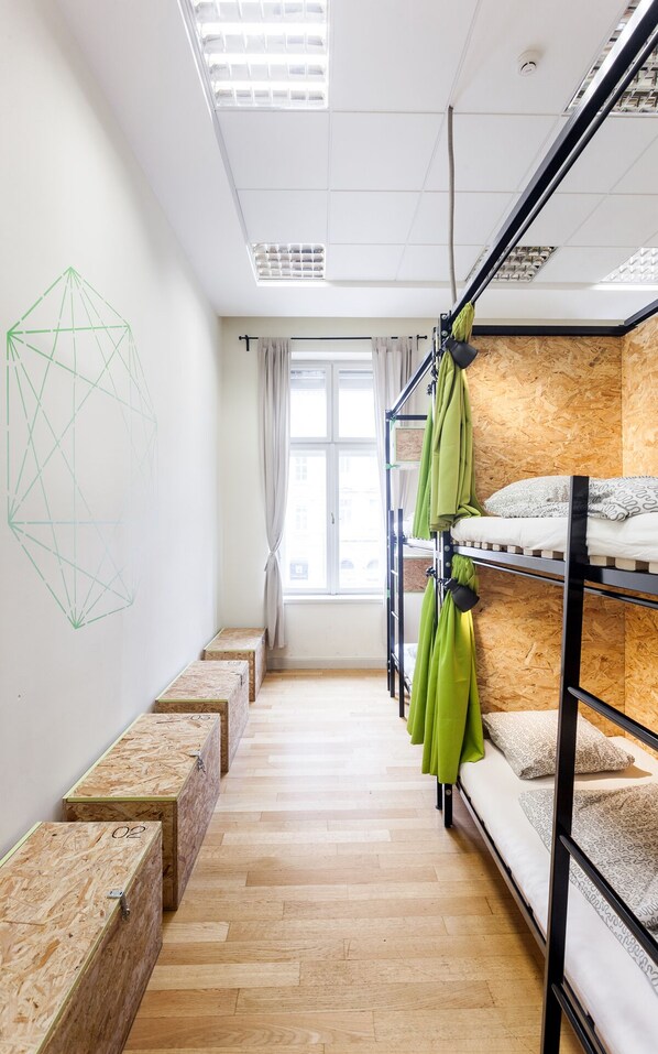 Un dormitorio con literas, un cuadro de arte geométrico, una ventana con cortinas y suelo de madera.