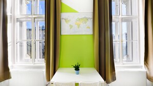 A room with a white table, two white chairs, a small blue plant, a world map on the wall, and large windows with curtains. - Avenue Hostel (Budapest)