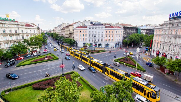 A city street with yellow trams, cars, and pedestrians. - Avenue Hostel (Budapest)