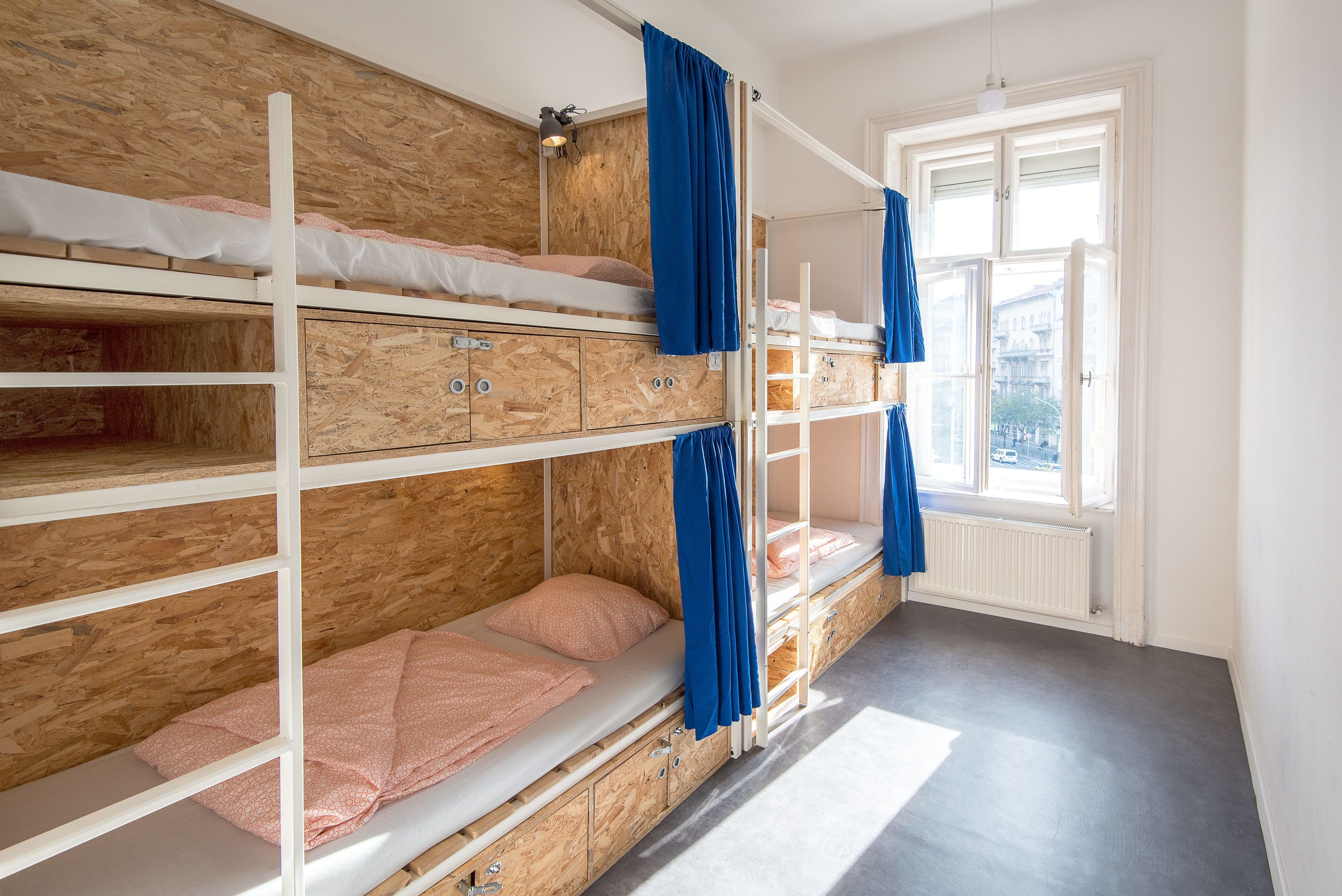 Een slaapkamer met een stapelbed, houten lambrisering, een raam met gordijnen en een radiator.