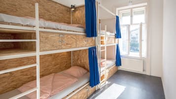 Een slaapkamer met een stapelbed, houten lambrisering, een raam met gordijnen en een radiator.