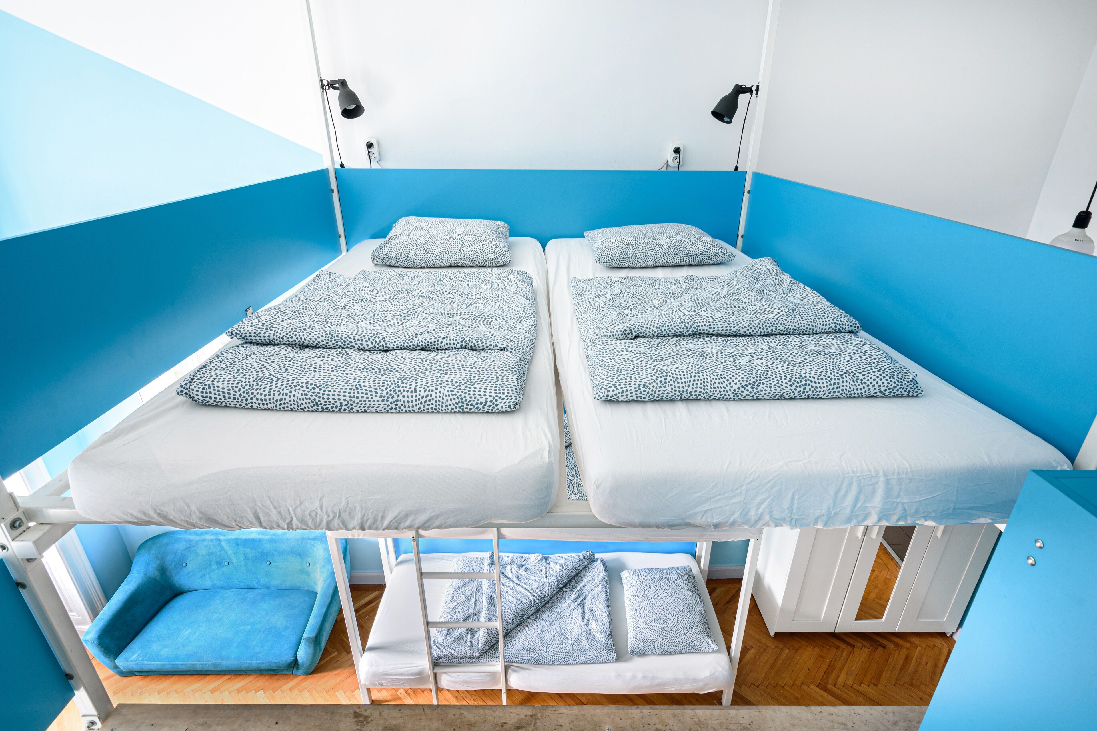 Una habitación con dos camas, cada una con un cojín estampado en azul y blanco, una silla azul y una escalera.